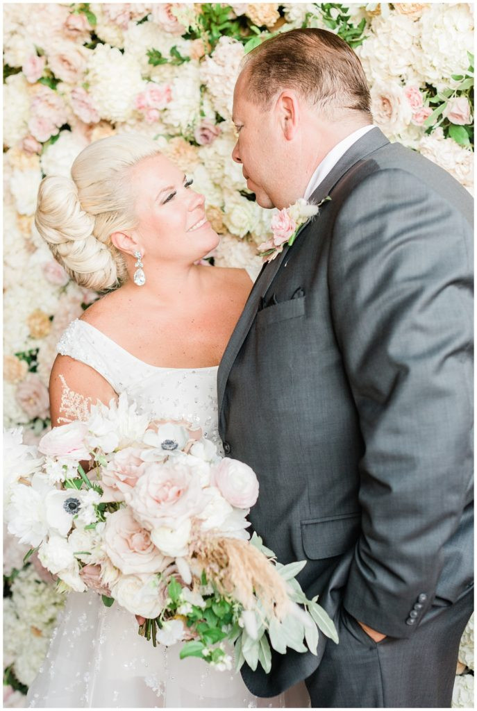 Bride and groom looking at each other in front of the flower wall at Teak Red Bank.